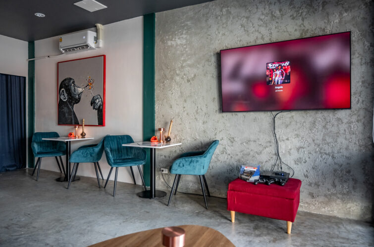 MR.WEED lounge with teal velvet chairs, a red ottoman and a large screen